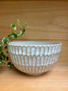 Bol Giwa en grès blanc fait main, design élégant avec motifs texturés, posé sur une surface en bois avec une plante décorative.