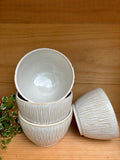 Ensemble de Bols Póa empilés, avec motifs herbe texturés, exposés sur une étagère en bois, parfaits pour un style organique.