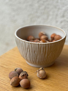 Bol Póa artisanal avec motifs herbe, rempli de noisettes, posé sur une table en bois clair, idéal pour une présentation naturelle.