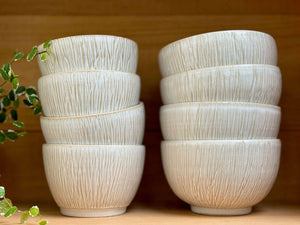 Deux piles de Bols Póa avec motifs herbe, exposées sur une étagère en bois, ajoutant une touche artisanale et naturelle à la cuisine.