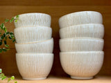 Deux piles de Bols Póa avec motifs herbe, exposées sur une étagère en bois, ajoutant une touche artisanale et naturelle à la cuisine.