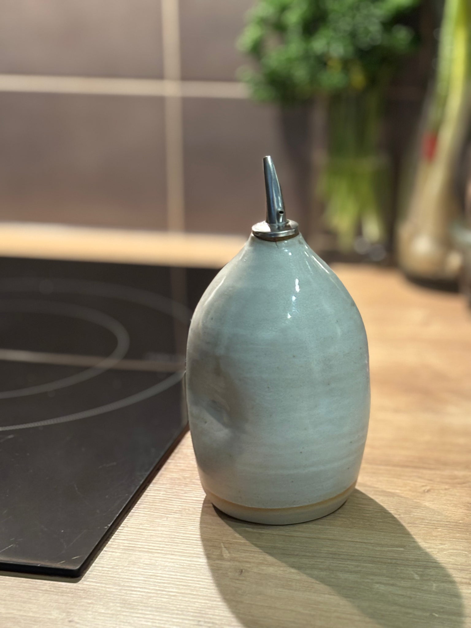 Huilier en céramique artisanale avec bec verseur en inox, posé sur un plan de travail en cuisine.
