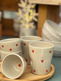 Mug et tasses en céramique artisanale avec motifs de cœurs rouges, présentés sur un plateau en bois