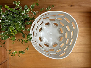 Vue de dessus du Panier Baguni en grès blanc, montrant ses motifs ajourés uniques, accompagné d'une plante verte sur une table en bois.