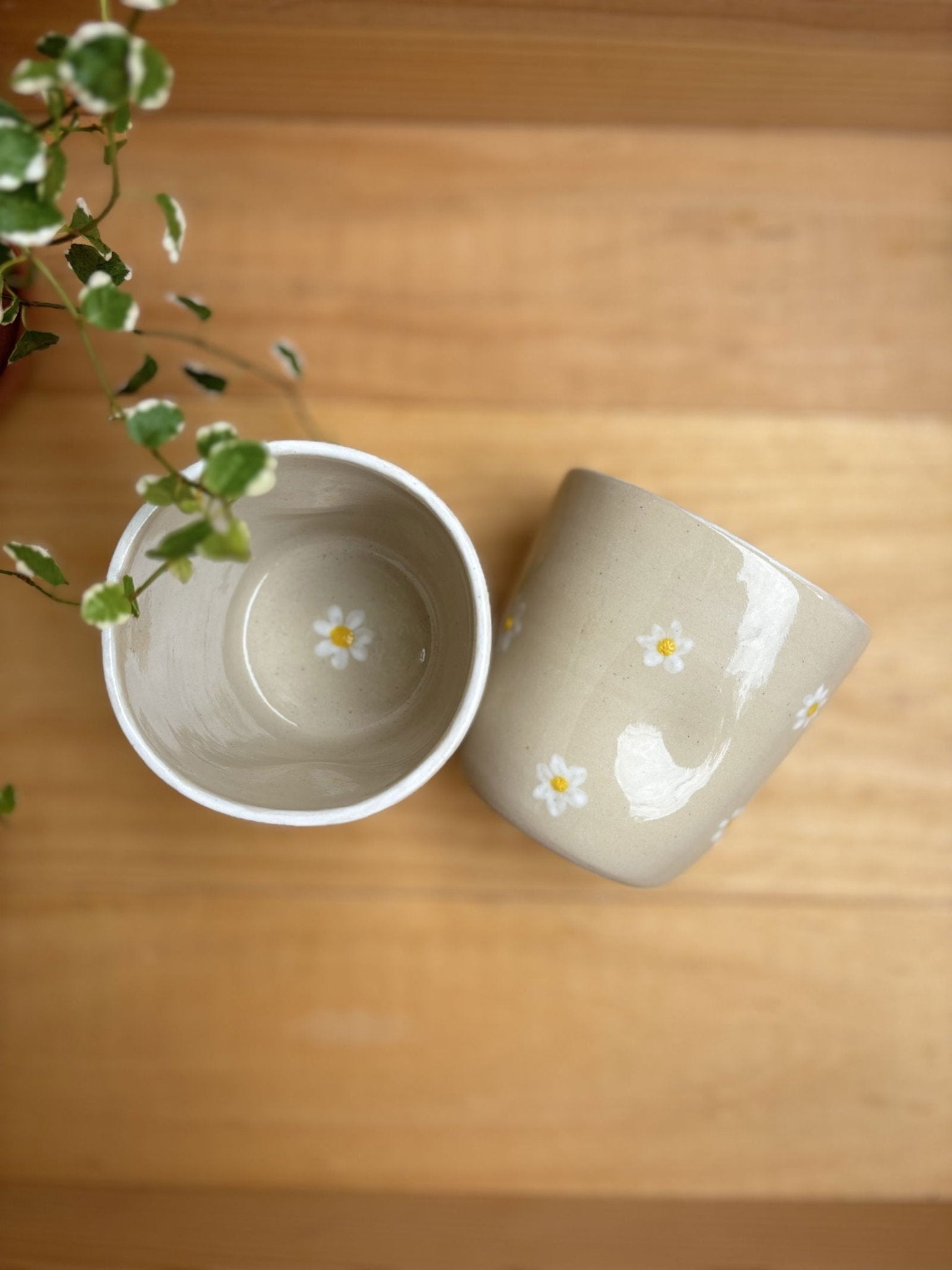Deux Tasses Marguerite artisanales en grès blanc avec motifs floraux, l'une vue de dessus et l'autre montrant l'extérieur décoré.