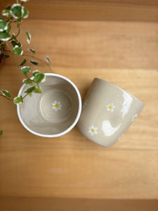 Deux Tasses Marguerite artisanales en grès blanc avec motifs floraux, l'une vue de dessus et l'autre montrant l'extérieur décoré.