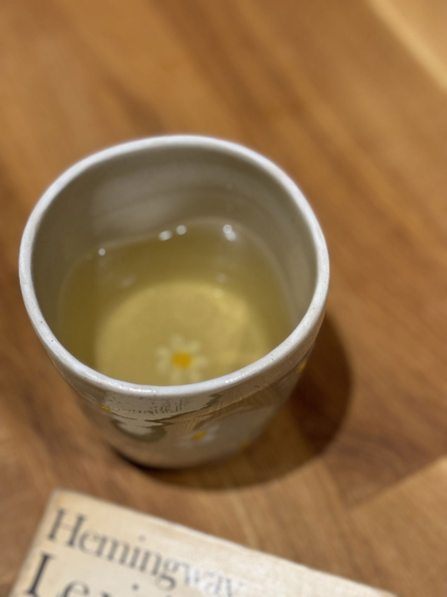 Tasse Marguerite artisanale en grès blanc avec motif de marguerites, remplie de thé, posée sur une table en bois clair.