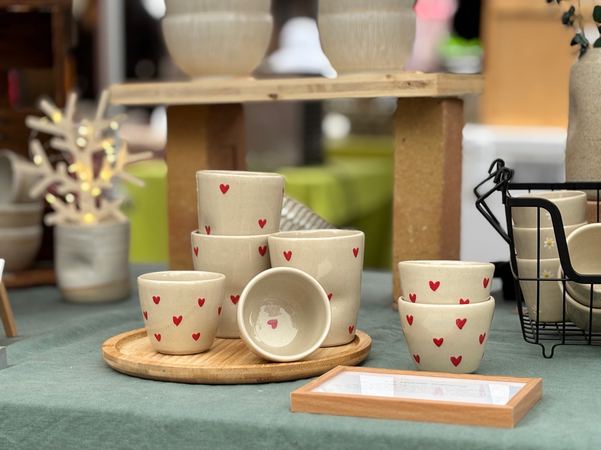 Tasses en céramique artisanale avec motifs de cœurs rouges, disposées sur un plateau en bois.