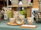 Tasses en céramique artisanale avec motifs de cœurs rouges, disposées sur un plateau en bois.