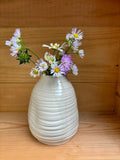 Vase Pado en céramique beige avec des fleurs sauvages colorées, placé sur une étagère en bois. Élégance artisanale pour votre maison.