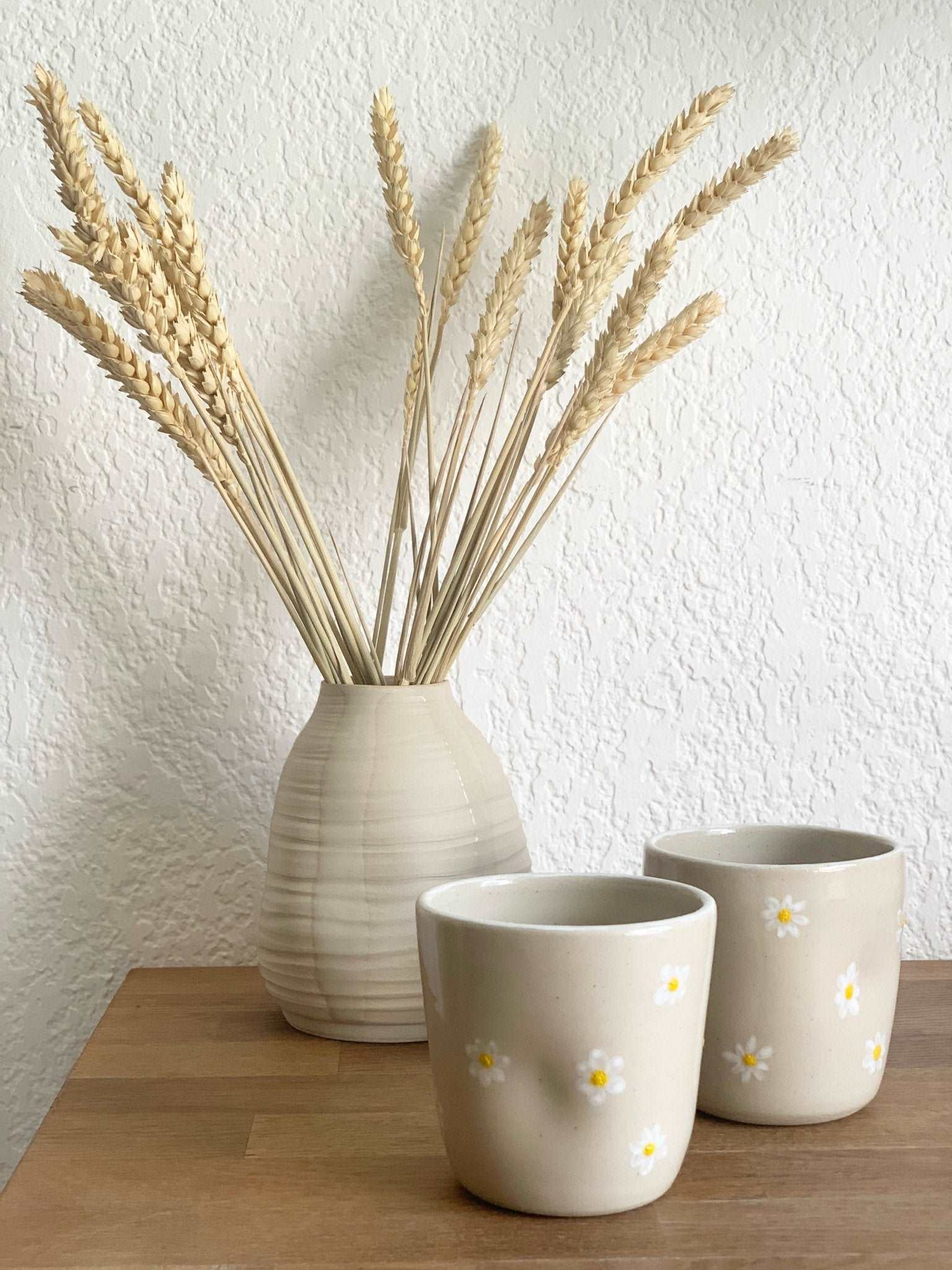 Vase Pado beige en céramique avec des épis de blé, accompagné de tasses décorées de fleurs blanches. Parfait pour un intérieur naturel.